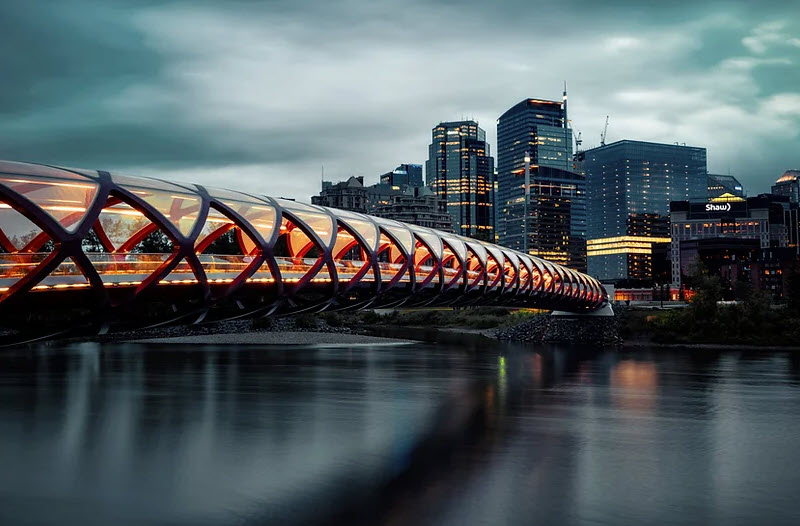 Een foto van een moderne voetgangersbrug met een overkapping van versterkt staal en glas.