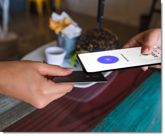 Persona colocando una tarjeta de crédito debajo de un teléfono para pagar con Tap to Pay